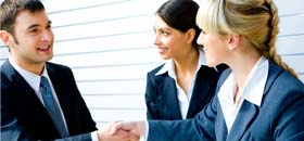 Photo of three people smiling, two of them shaking hands